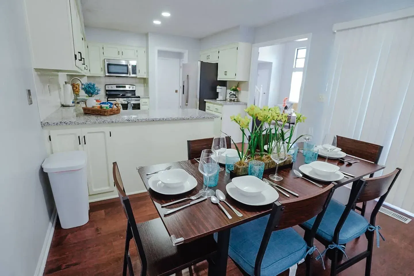 A dining room table with plates , utensils , and blue chairs in a kitchen.
