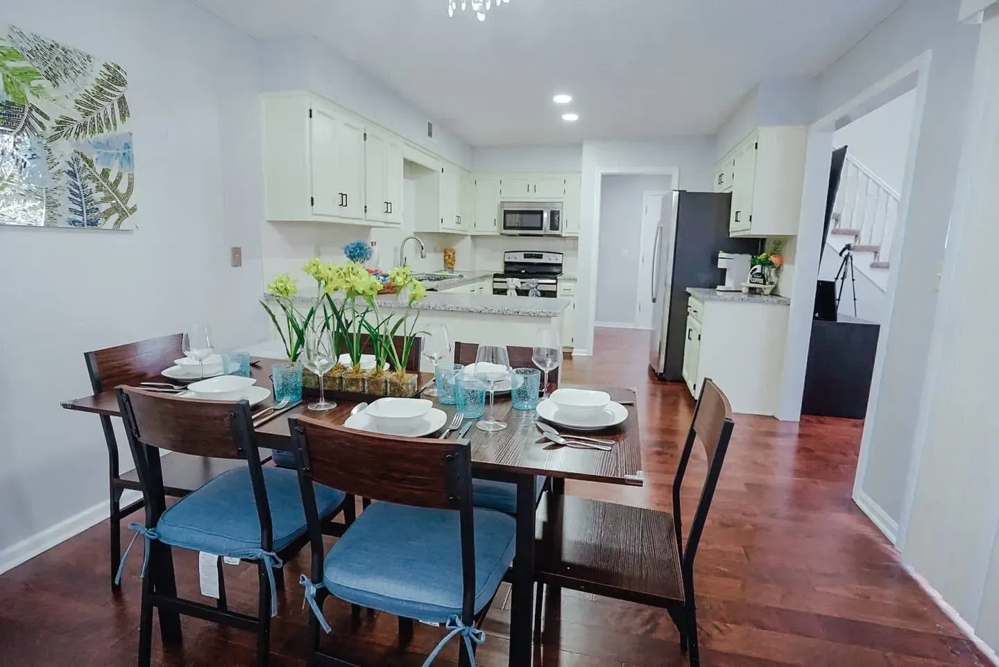 A dining room with a table and chairs and a kitchen in the background.
