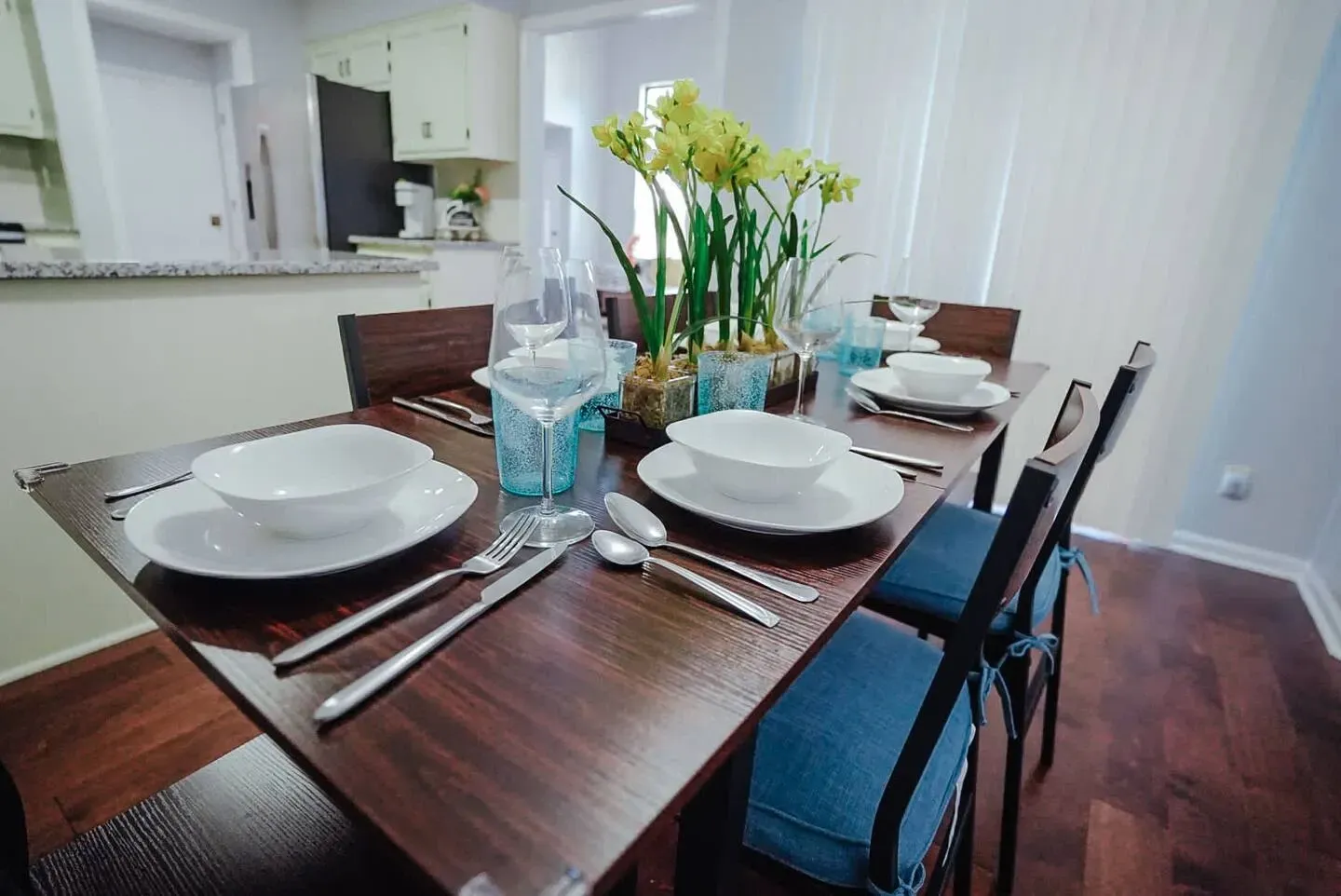 A dining room table with plates , bowls , silverware and a vase of flowers on it.