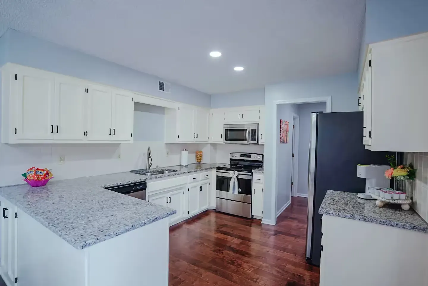 A kitchen with white cabinets , granite counter tops , stainless steel appliances and hardwood floors.