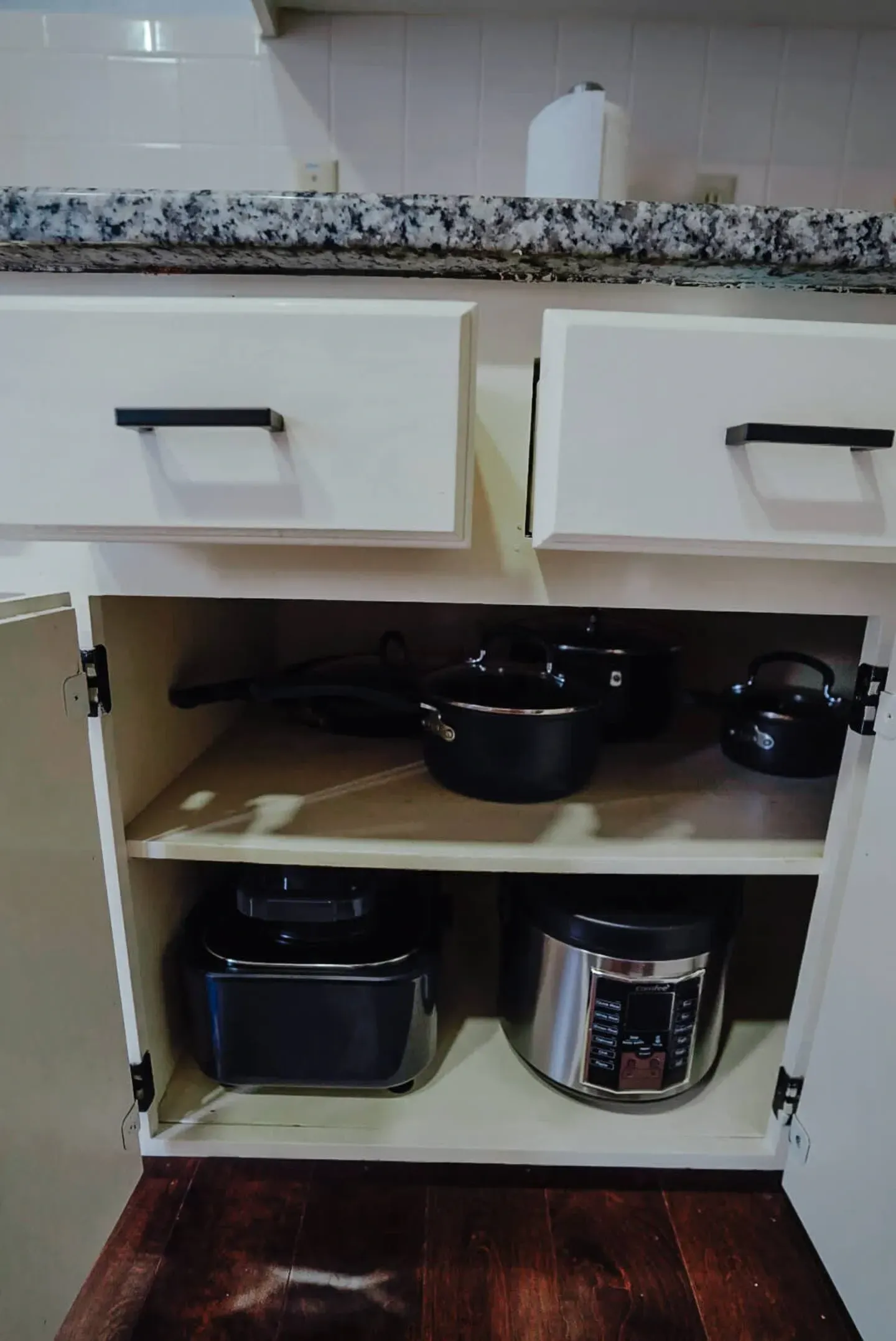 A kitchen cabinet filled with pots and pans and a toaster oven.