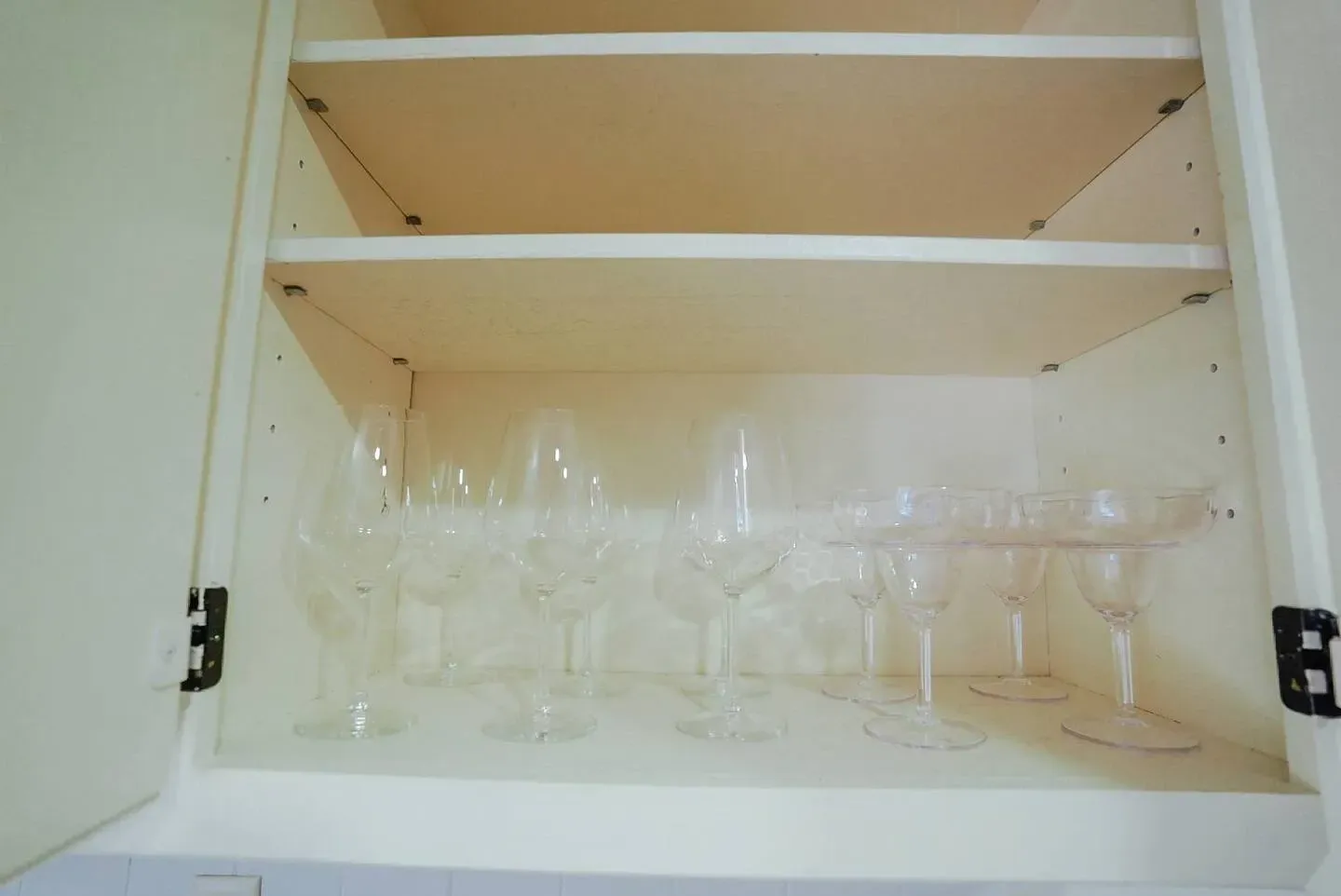 A bunch of wine glasses are sitting on a shelf in a cabinet.