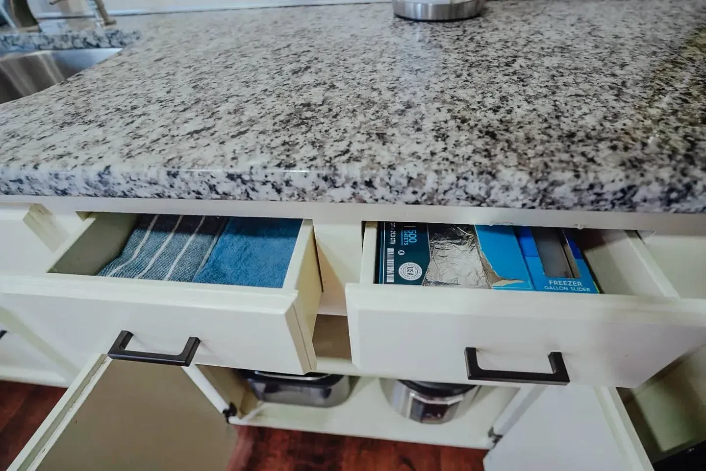 A kitchen counter with two drawers open and a blue towel in one drawer