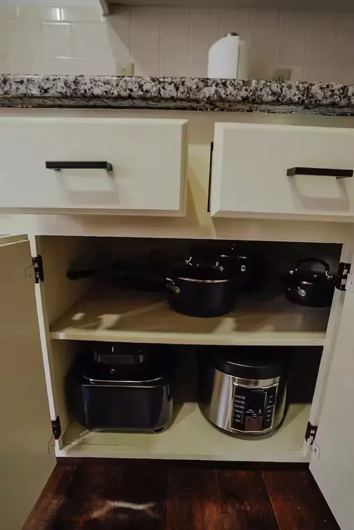 A kitchen cabinet filled with pots and pans and a toaster oven.