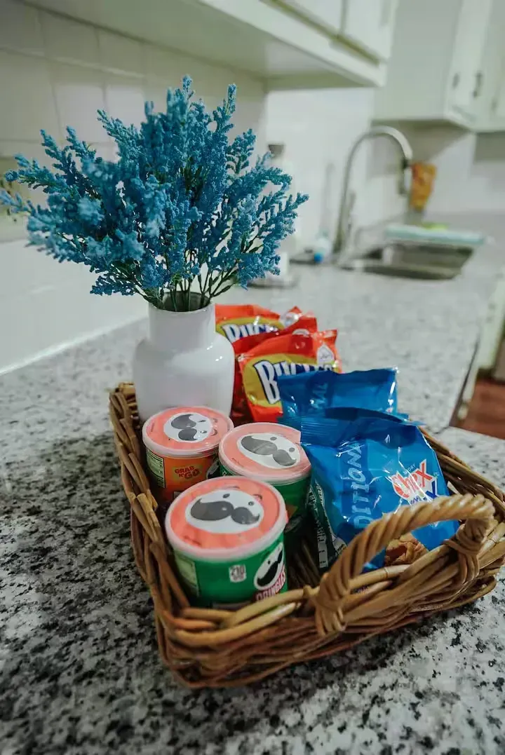 A wicker basket filled with snacks and a vase of flowers on a kitchen counter.