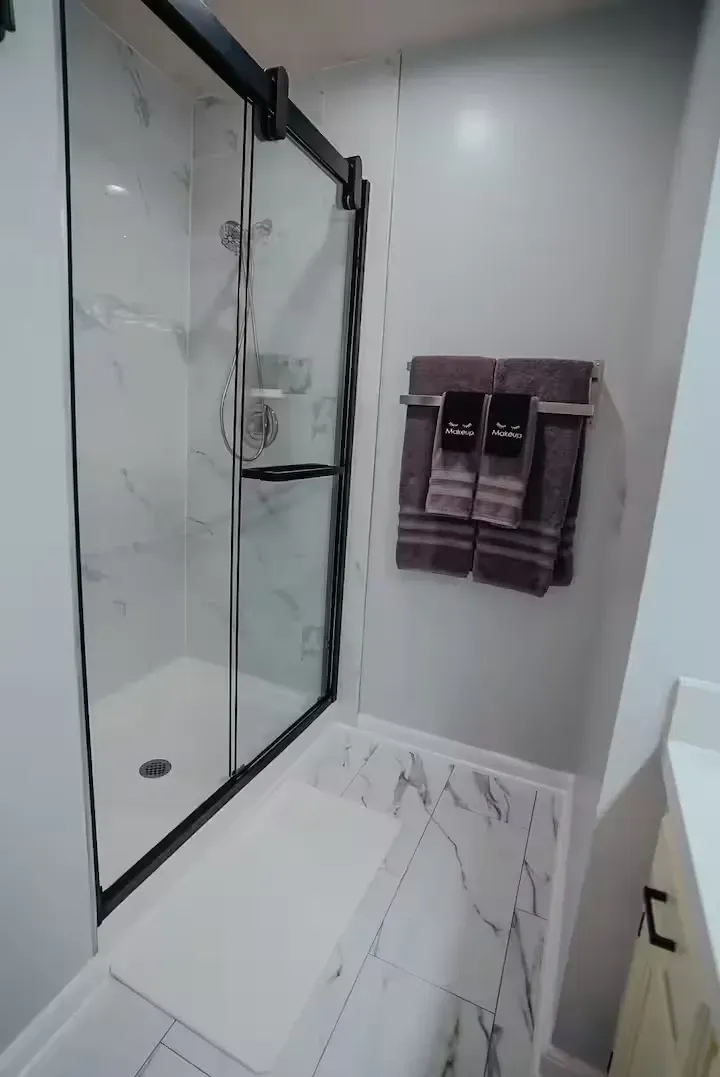 A bathroom with a walk in shower and two towels hanging on the wall.