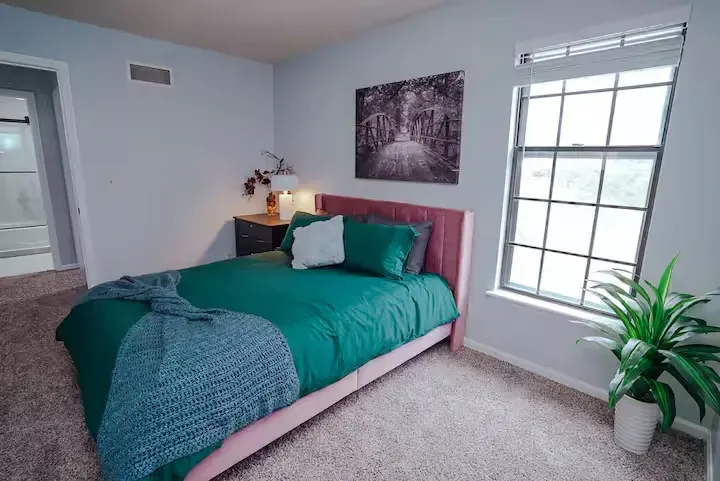A bedroom with a bed , window and plant.