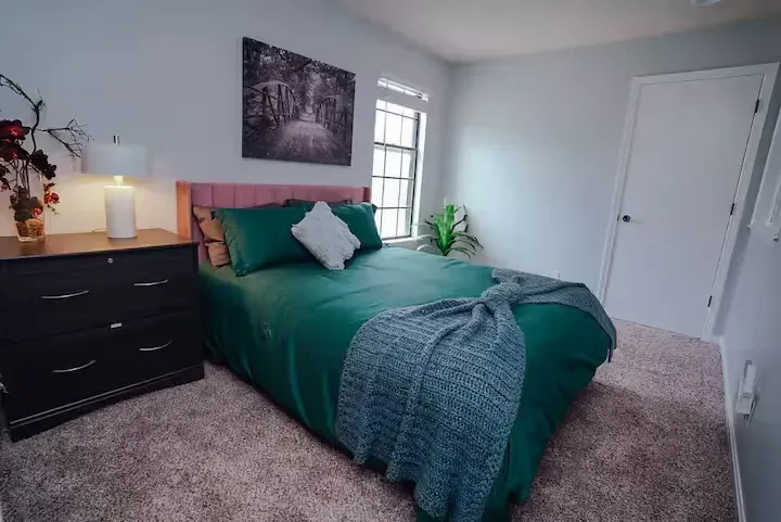 A bedroom with a bed , dresser , lamp and window.