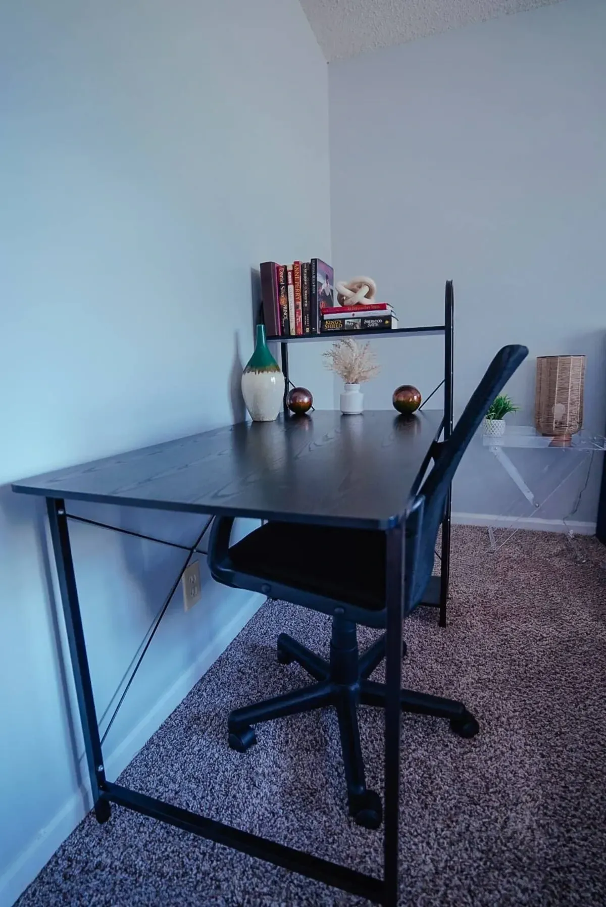 A black desk and chair in a room with a bookshelf.