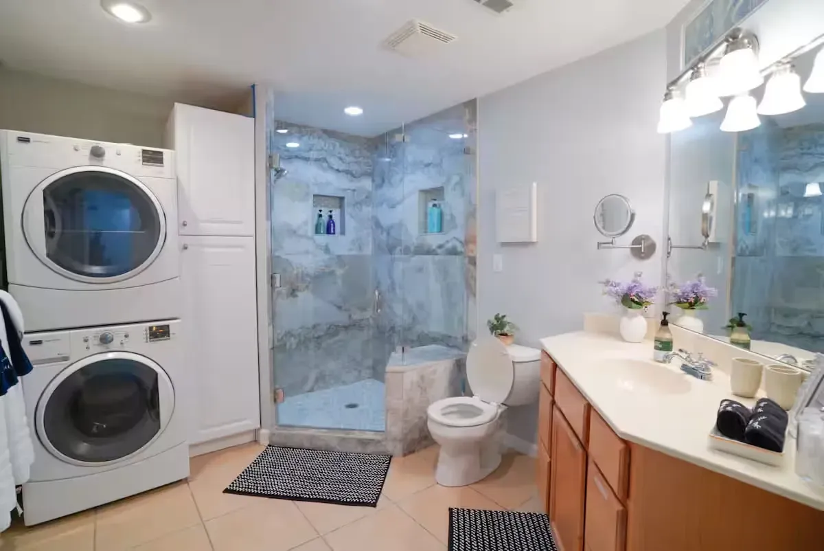 A bathroom with a washer and dryer stacked on top of each other and a toilet.