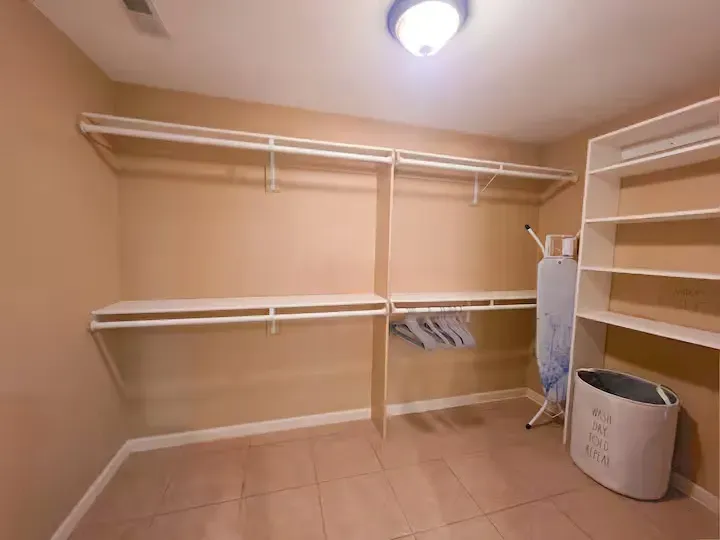 An empty walk in closet with a laundry basket and ironing board.