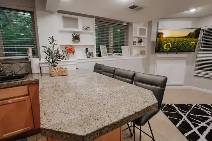 A kitchen with a granite counter top and a flat screen tv on the wall.