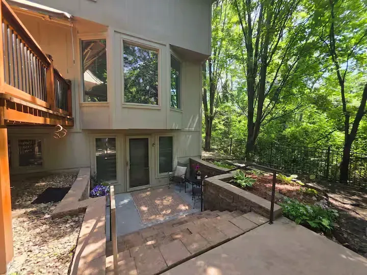A house with a patio and stairs leading up to it surrounded by trees.