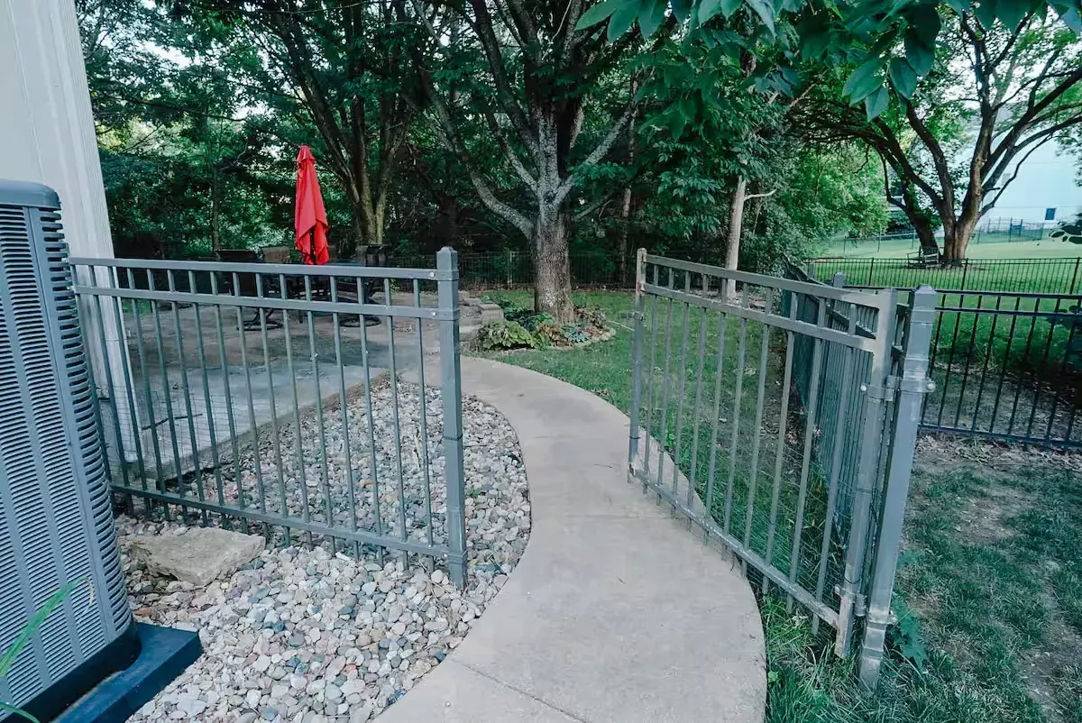 A metal fence surrounds a walkway leading to a patio.
