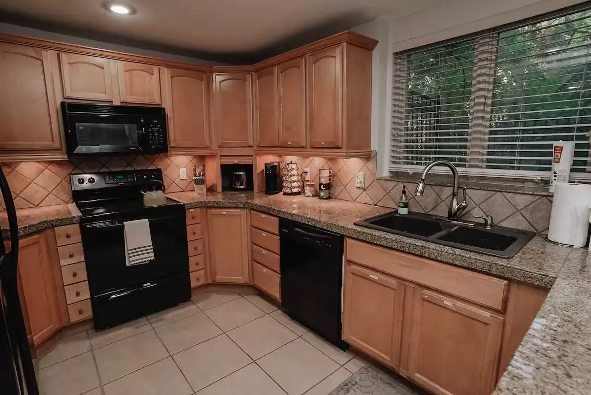 A kitchen with wooden cabinets , black appliances , granite counter tops and a window.
