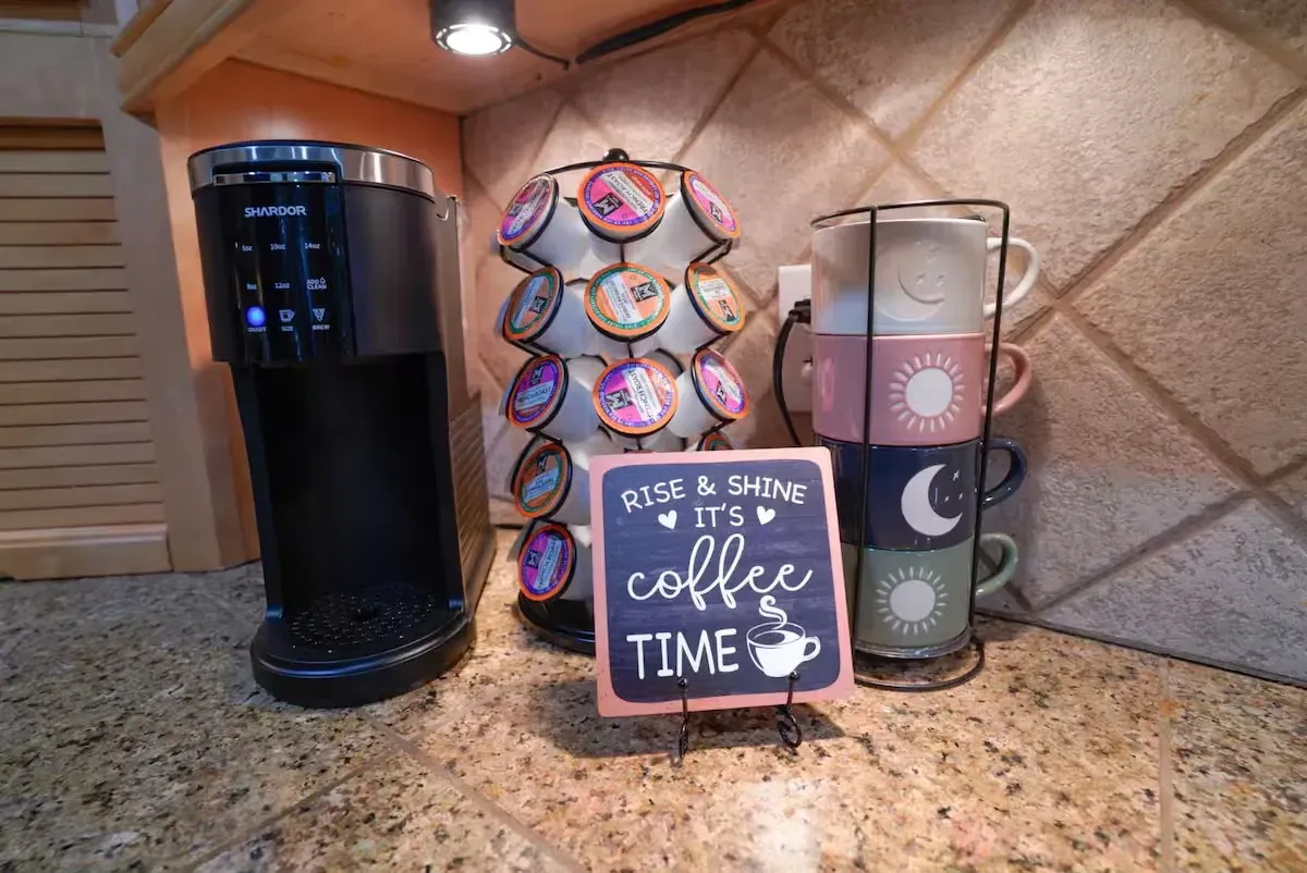 A coffee maker is sitting on a counter next to a sign that says `` rise and shine it 's coffee time ''.