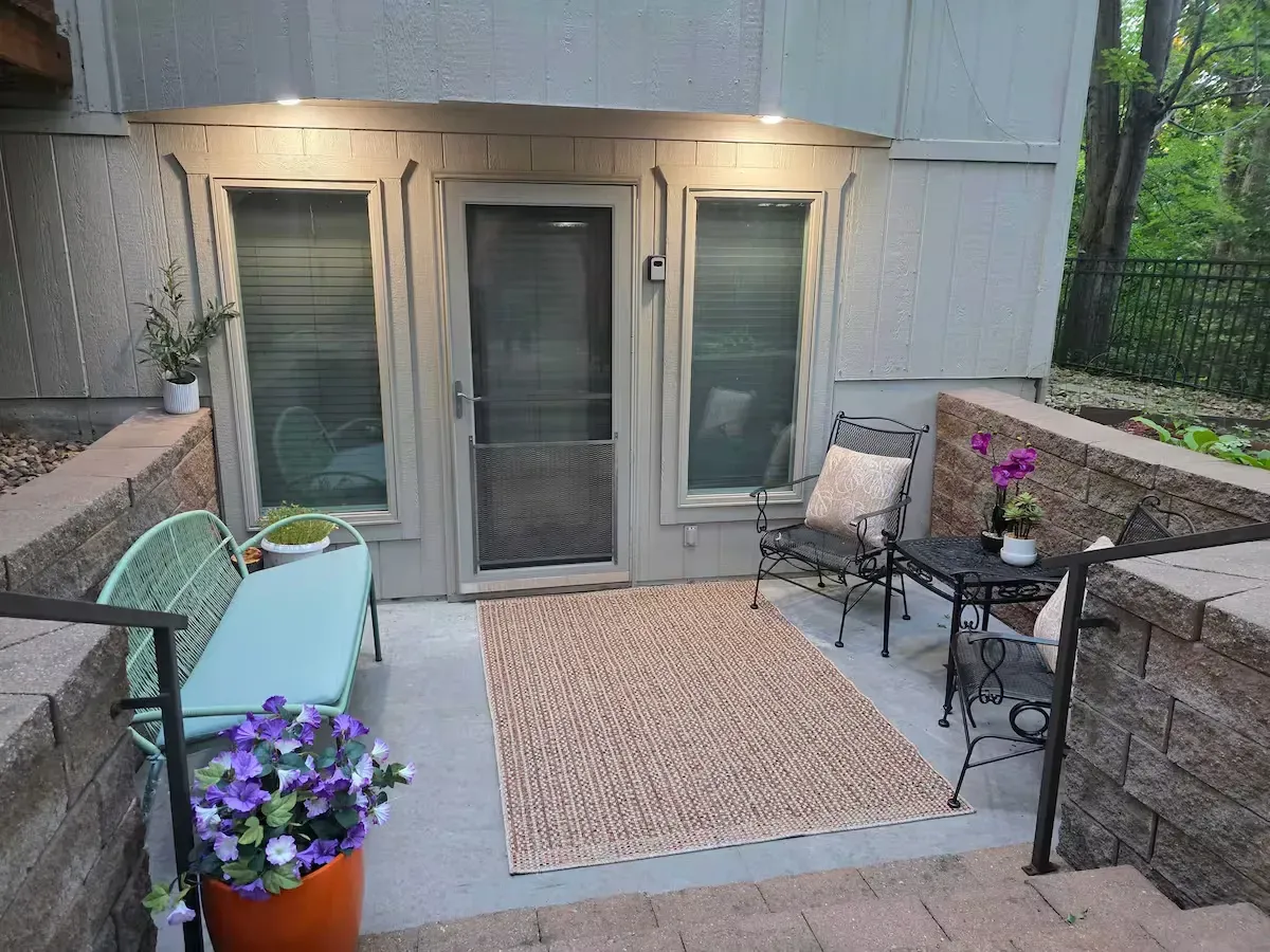 A patio with a bench , chairs , table and flowers.
