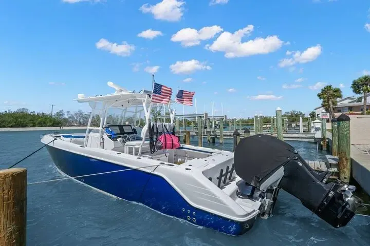 A blue and white motorboat docked at a wooden pier with American flags waving on a sunny day.