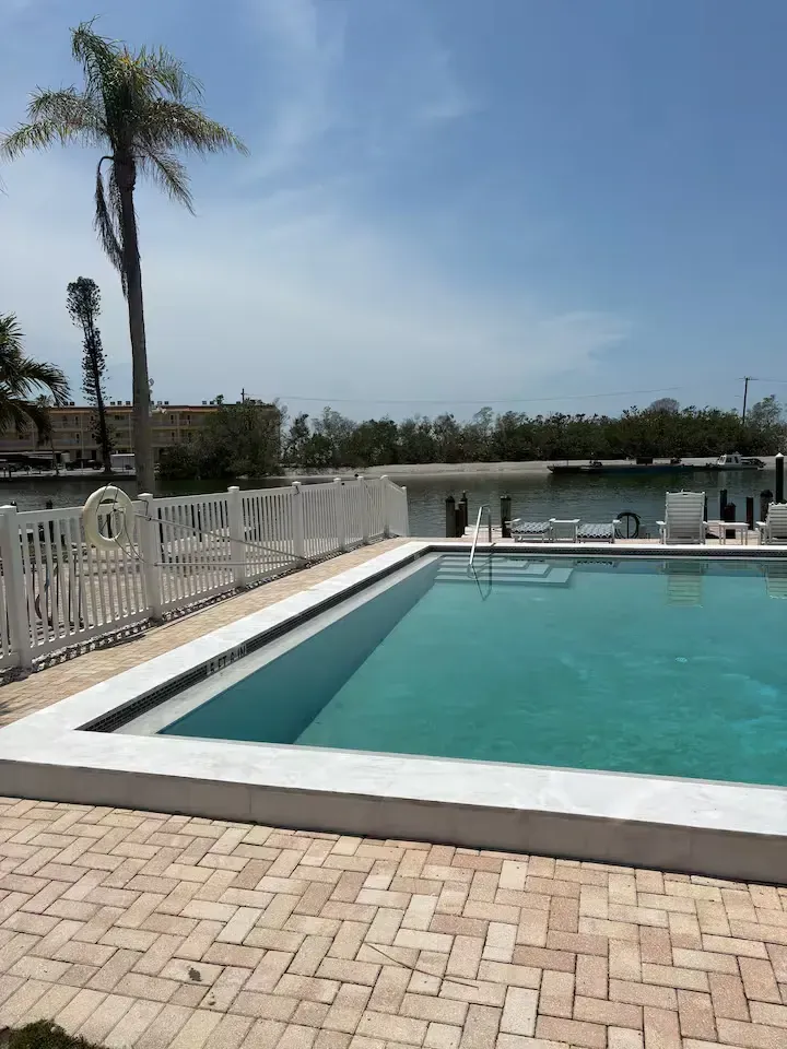 A rectangular swimming pool with clear turquoise water is enclosed by a white fence on a sunny day.