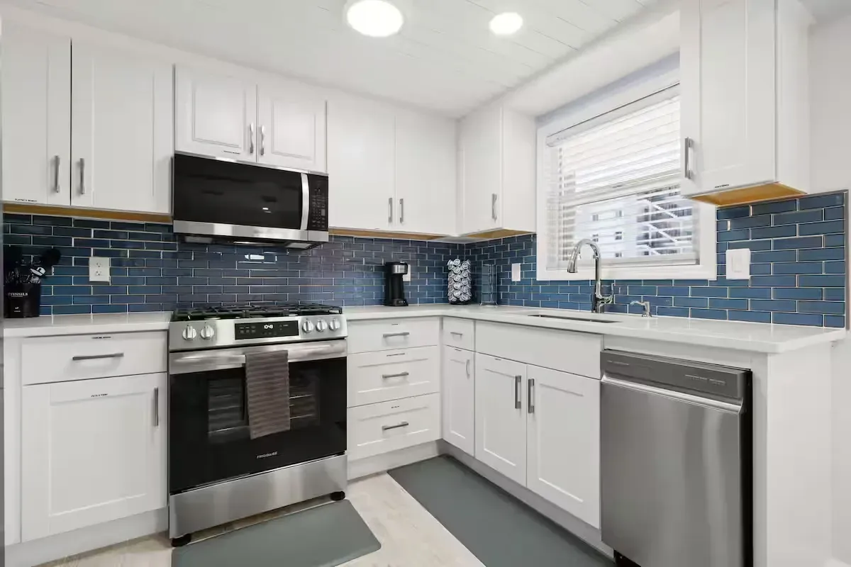 Bright white kitchen with stainless steel appliances, white cabinets, and blue tile backsplash.