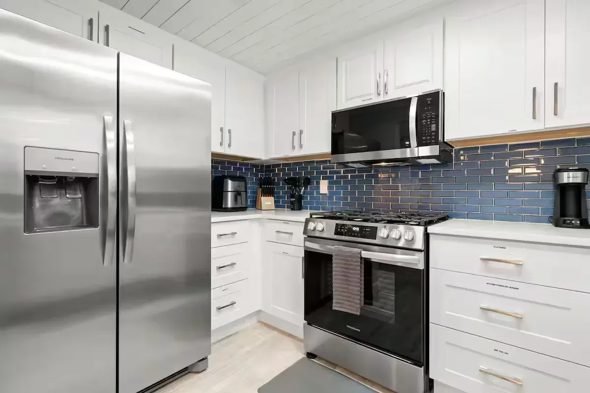 Stainless steel appliances in a small, white kitchen. A blue tiled backsplash accents the oven and microwave.