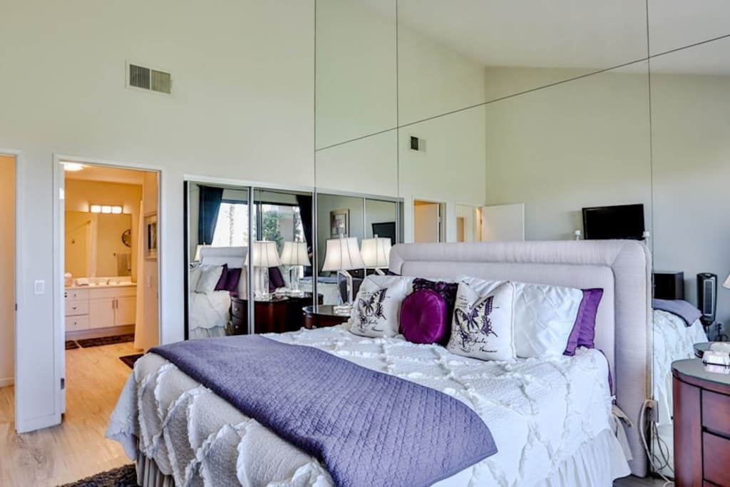 A bedroom with a large bed , mirrors on the wall , and a bathroom.- California- Trip- Summer