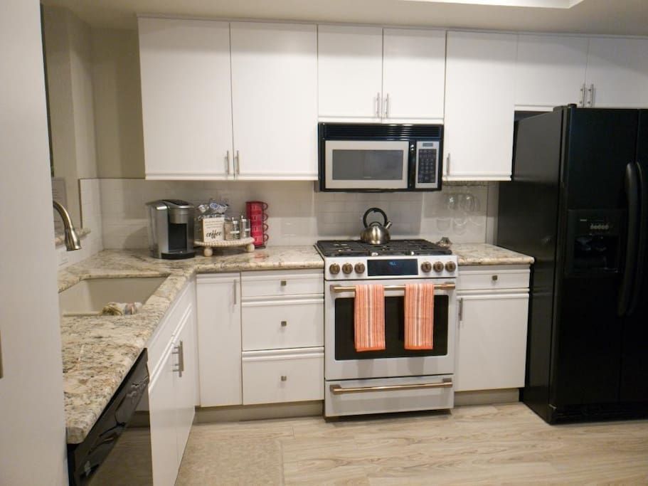 A kitchen with white cabinets , a black refrigerator , a stove , a microwave , and a sink.- California- Trip- Summer