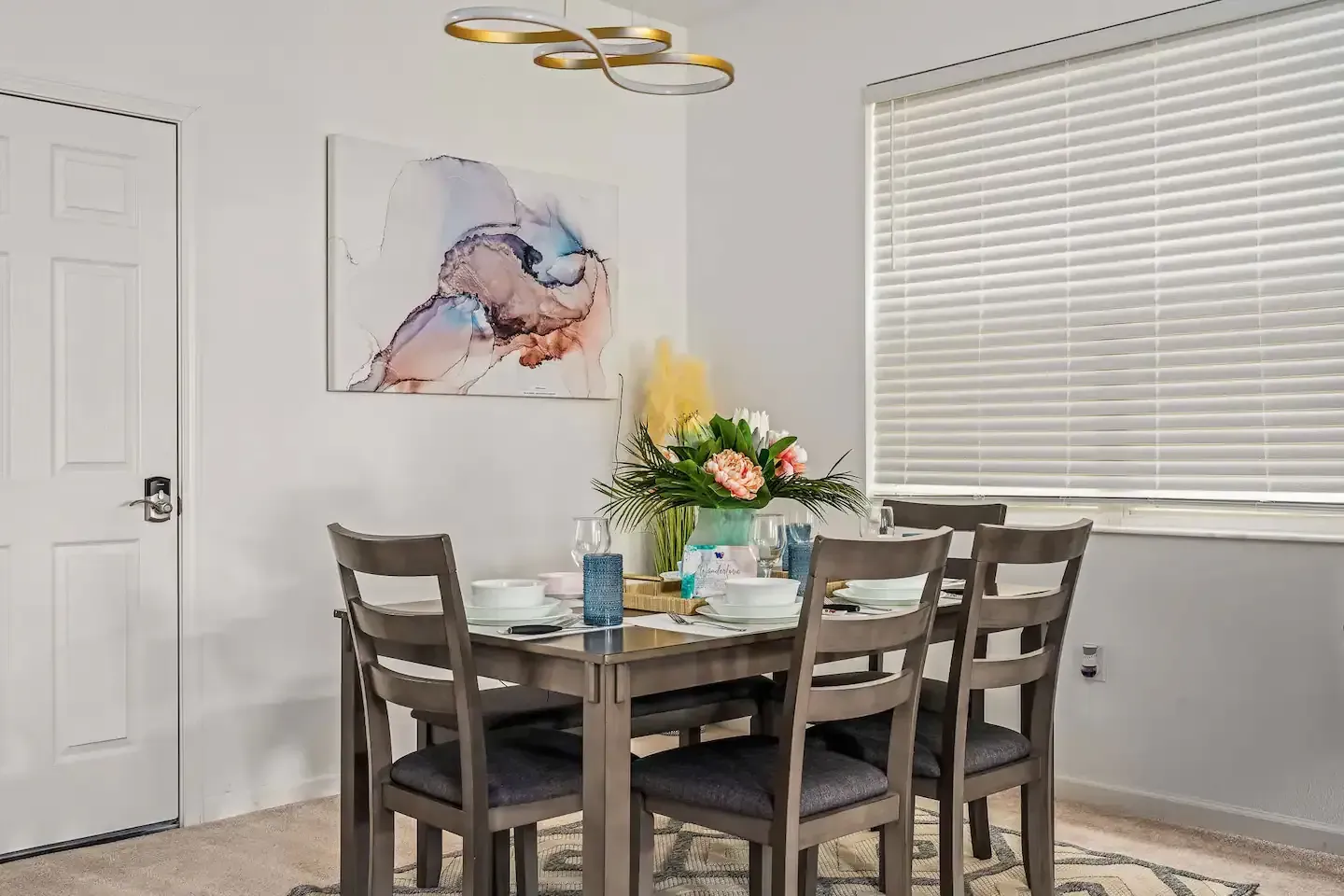 A dining room with a table and chairs and a painting on the wall.