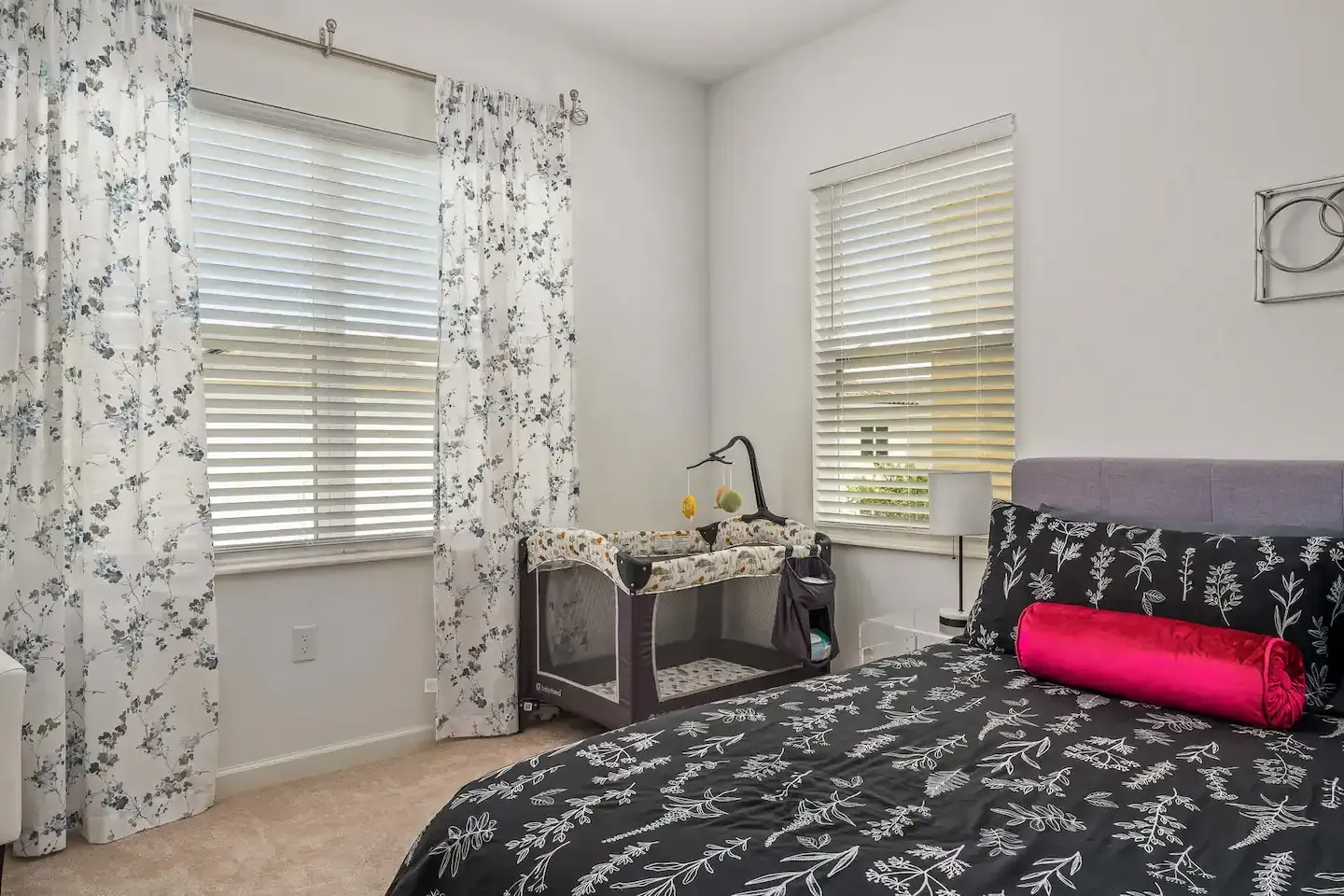 A bedroom with a bed , crib and two windows.