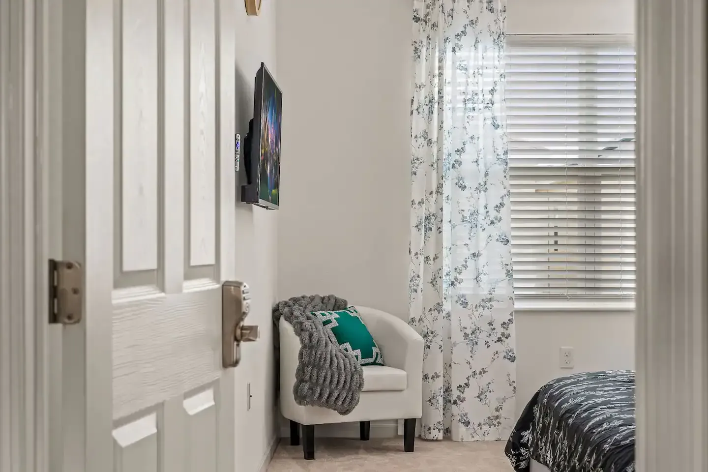 A bedroom with a bed , chair , television and blinds.