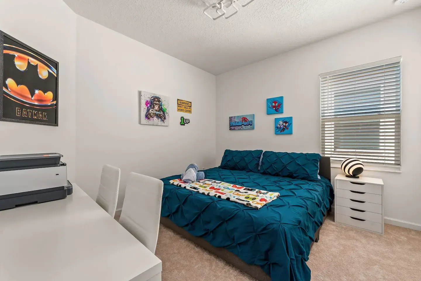 A bedroom with a bed , desk , chairs and a batman poster on the wall.