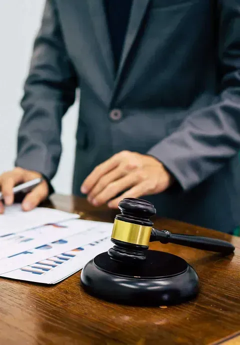 Una persona con traje junto a un mazo y documentos con gráficos, sobre una mesa de madera.