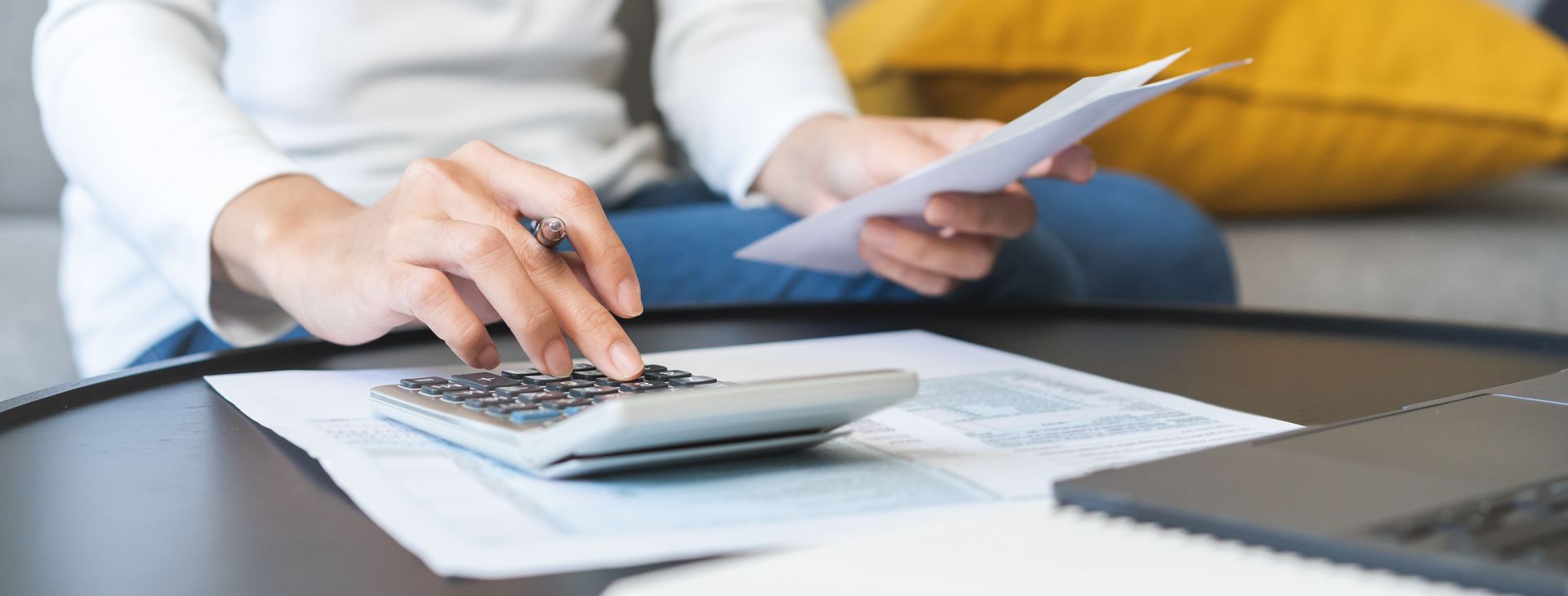 Apotheke kaufen: Eine Person benutzt einen Taschenrechner, während sie Unterlagen in der Hand hält, möglicherweise um Finanzdaten zu prüfen; ein Laptop befindet sich in der Nähe.