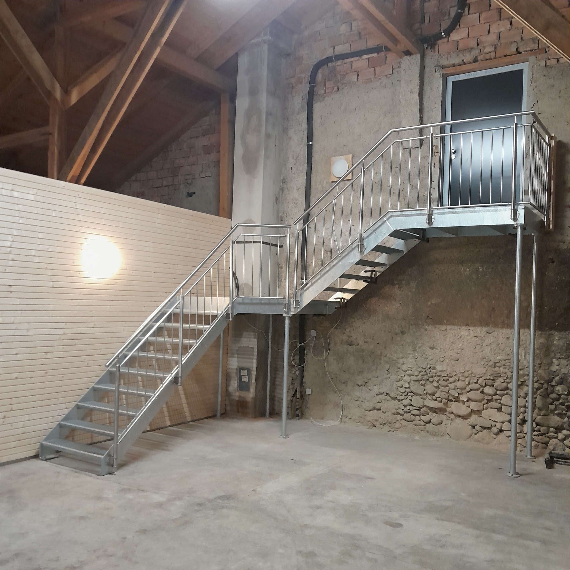 Ansicht Seite: Verzinkte Innentreppe bestehend aus Zwischenpodest, eingeschraubten Gitterroststufen und einem einseitig geführten Brüstungsgeländer aus geschliffenen Edelstahl. Die Abstützung erfolgte durch vertikale Rundsäulen aus verzinkten Stahl.