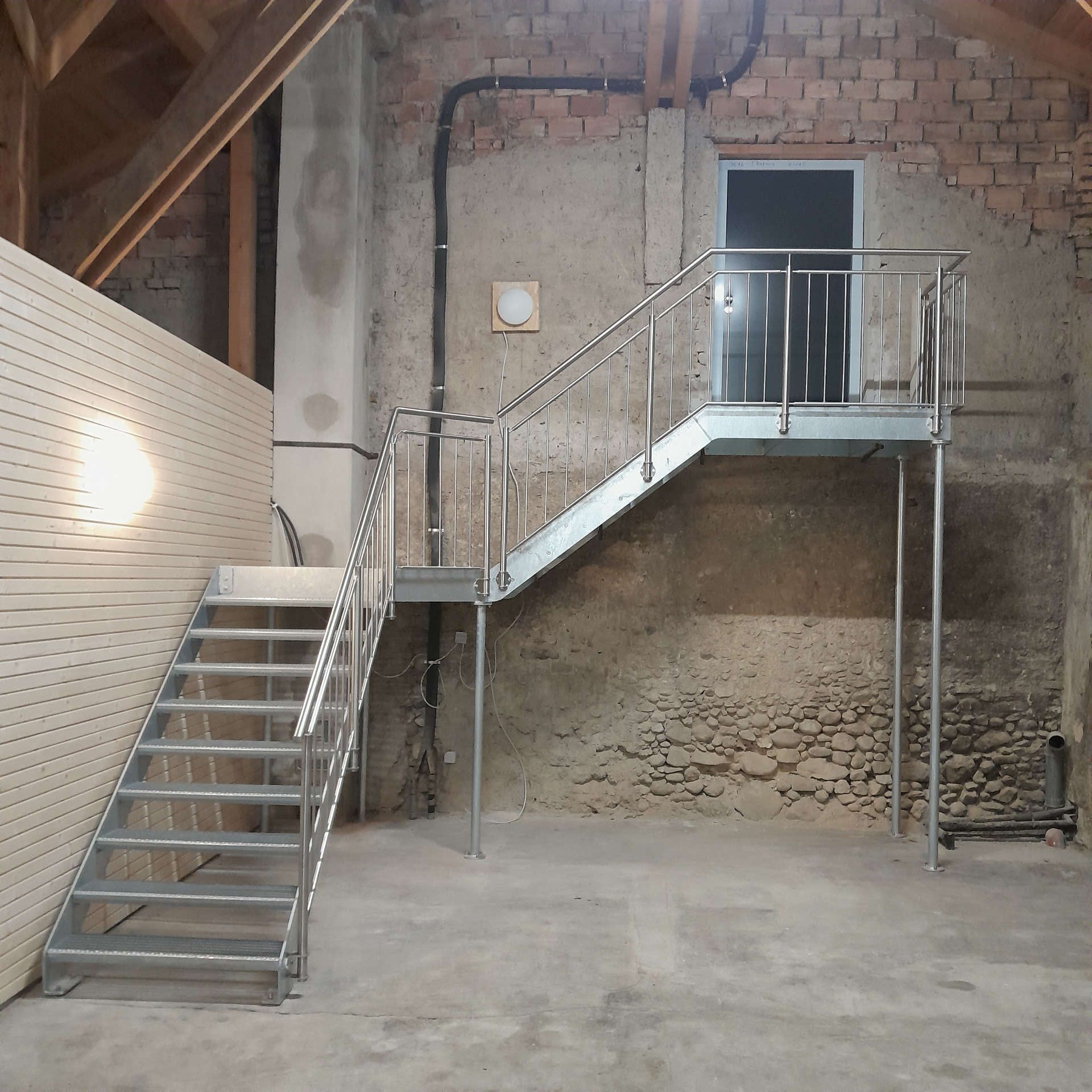 Ansicht Front: Verzinkte Innentreppe bestehend aus Zwischenpodest, eingeschraubten Gitterroststufen und einem einseitig geführten Brüstungsgeländer aus geschliffenen Edelstahl. Die Abstützung erfolgte durch vertikale Rundsäulen aus verzinkten Stahl.