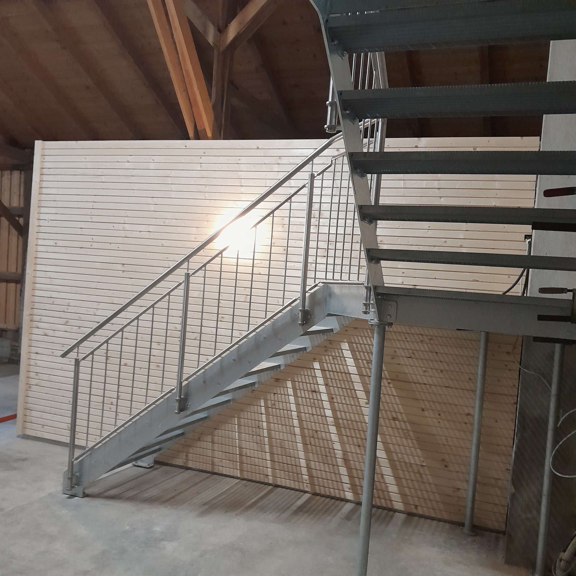 Ansicht unten drunter: Verzinkte Innentreppe bestehend aus Zwischenpodest, eingeschraubten Gitterroststufen und einem einseitig geführten Brüstungsgeländer aus geschliffenen Edelstahl. Die Abstützung erfolgte durch vertikale Rundsäulen aus verzinkten Stahl.
