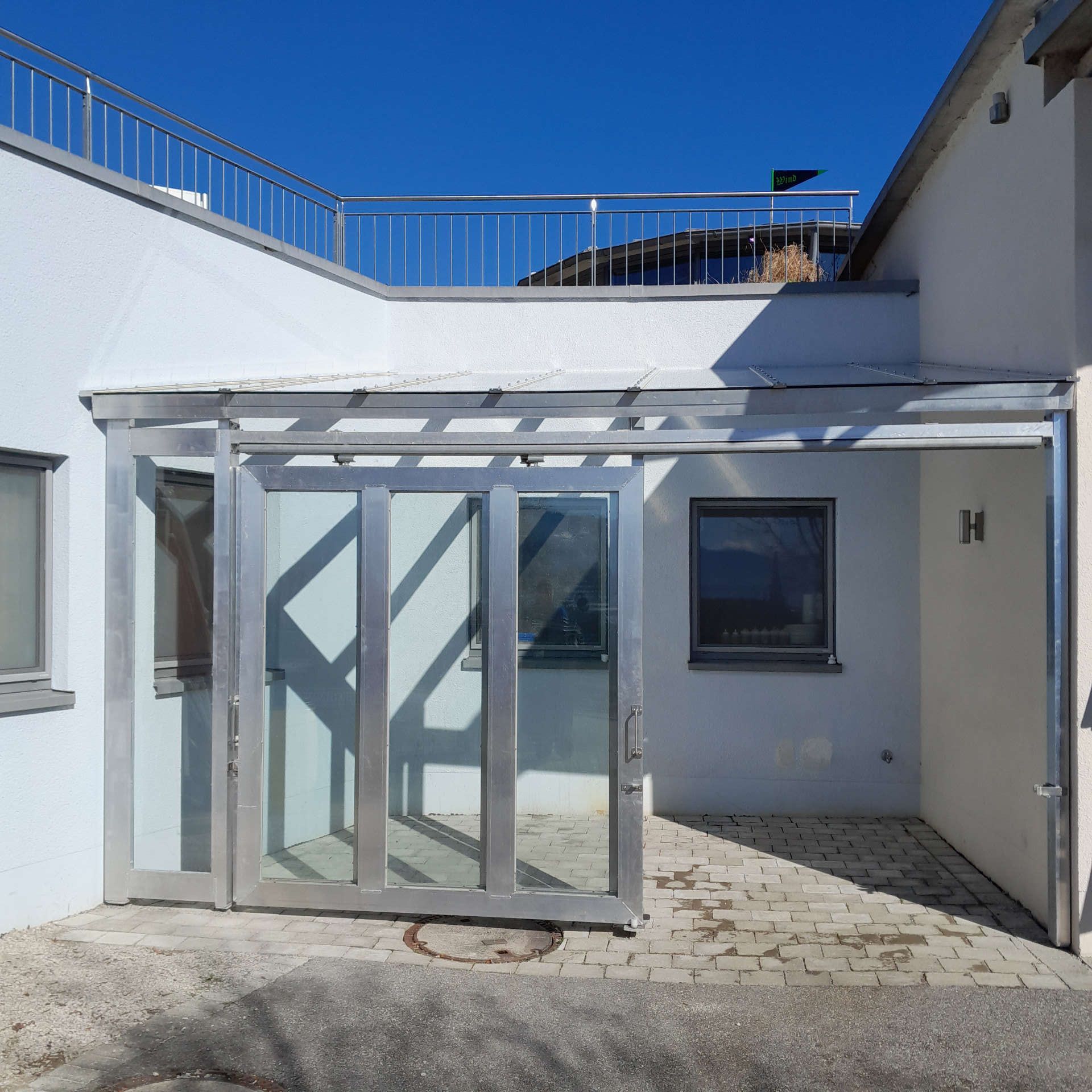 Vordachkonstruktion mit zwei Frontschiebetüren aus Aluminium mit Festverglasung und geöffneten Türen von außen