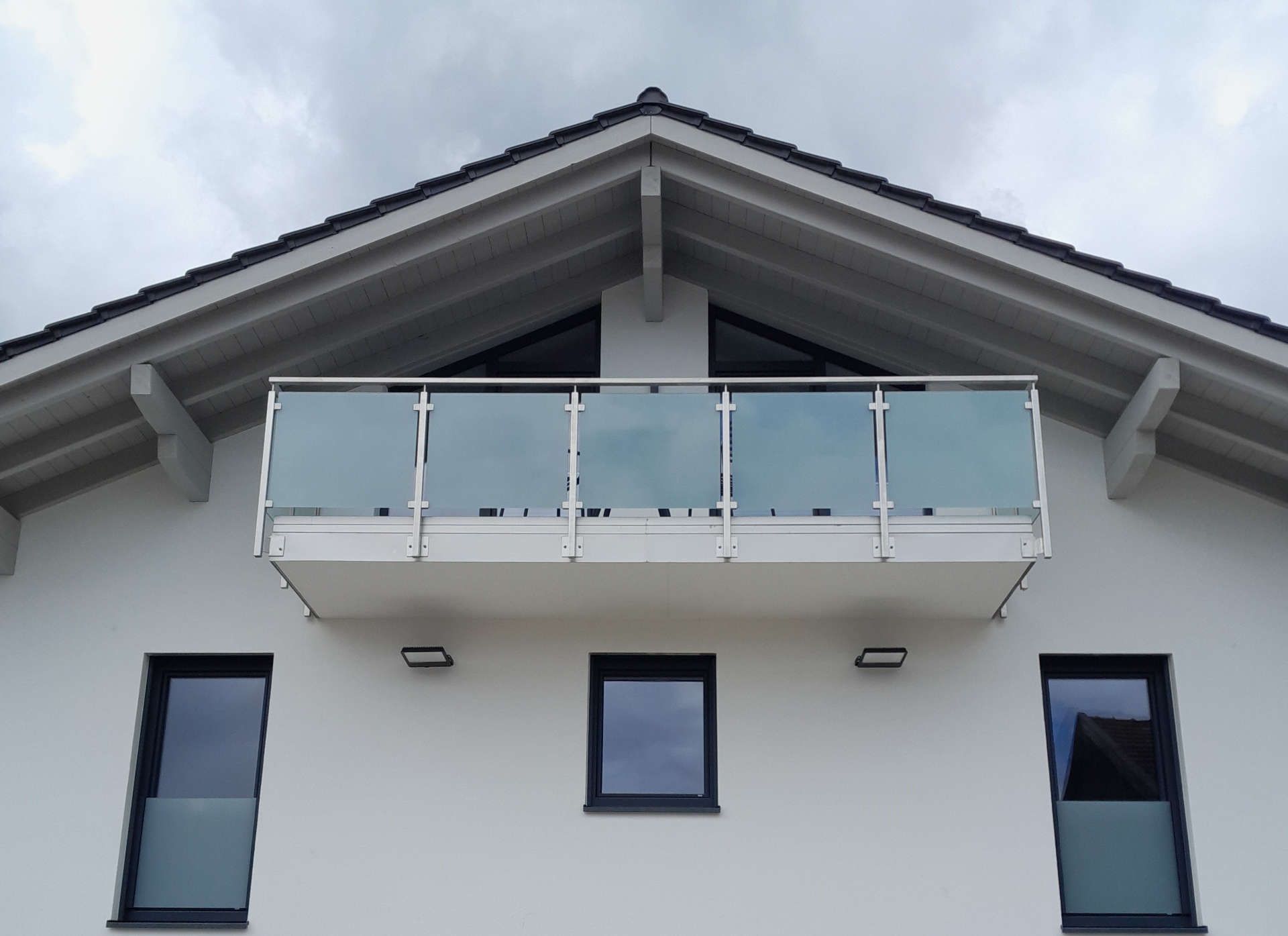 Ein weißes Haus mit einem Balkon direkt unter dem Dach (Frontalansicht)