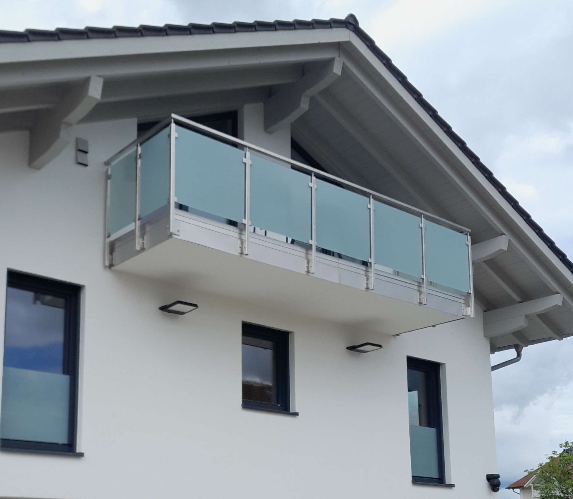 Ein weißes Haus mit einem Balkon direkt unter dem Dach (Schrägansicht)