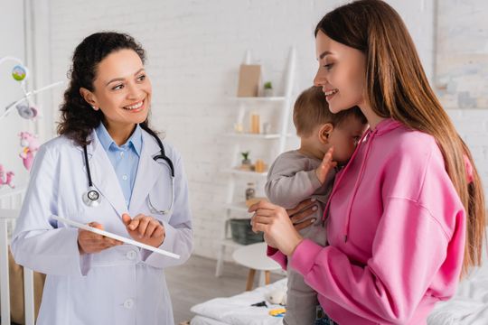 Una mujer sostiene un bebé y habla con un médico.