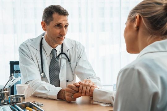 Un médico sostiene la mano de una paciente mientras habla con ella.
