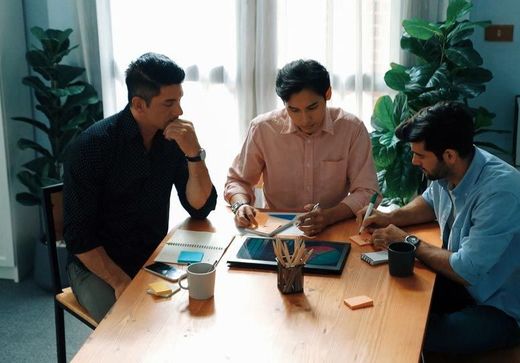 Tres hombres están sentados en una mesa teniendo una reunión.