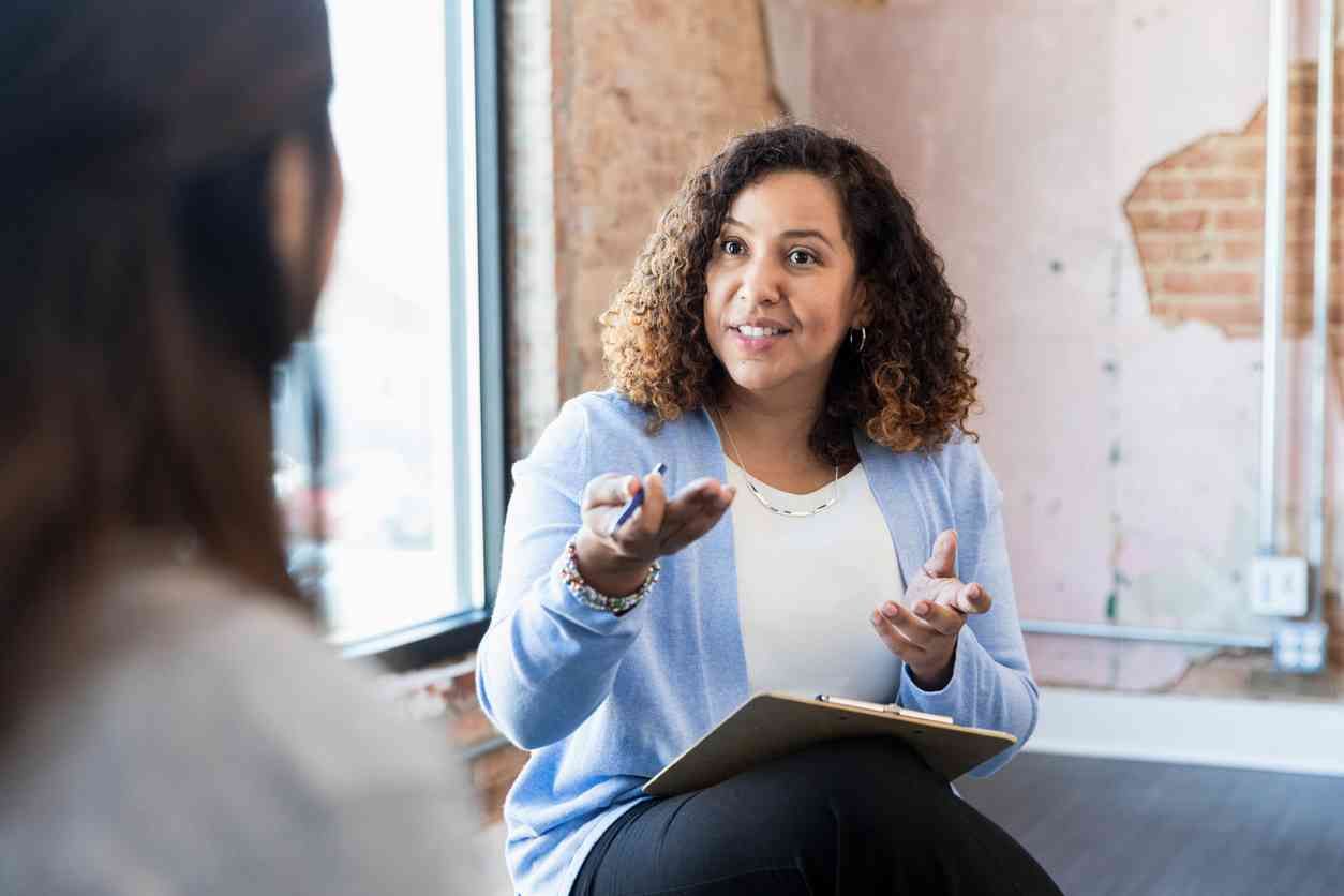 Una mujer está sentada en un sofá hablando con otra mujer.