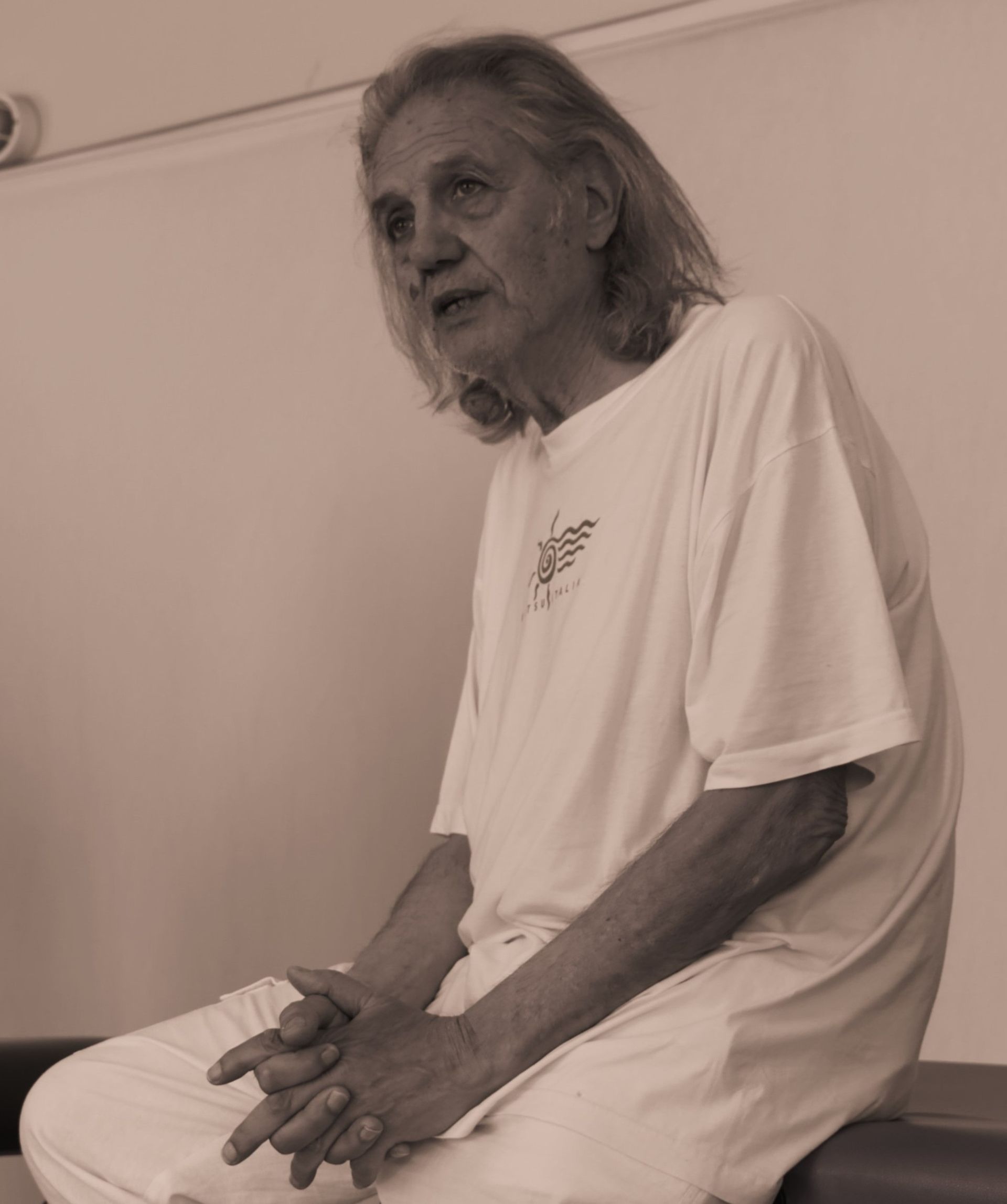Un hombre con una camisa blanca está sentado en un banco con las manos cruzadas.