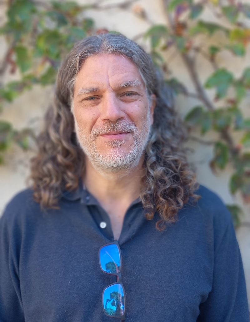 Un hombre con pelo largo y rizado y barba lleva gafas de sol.