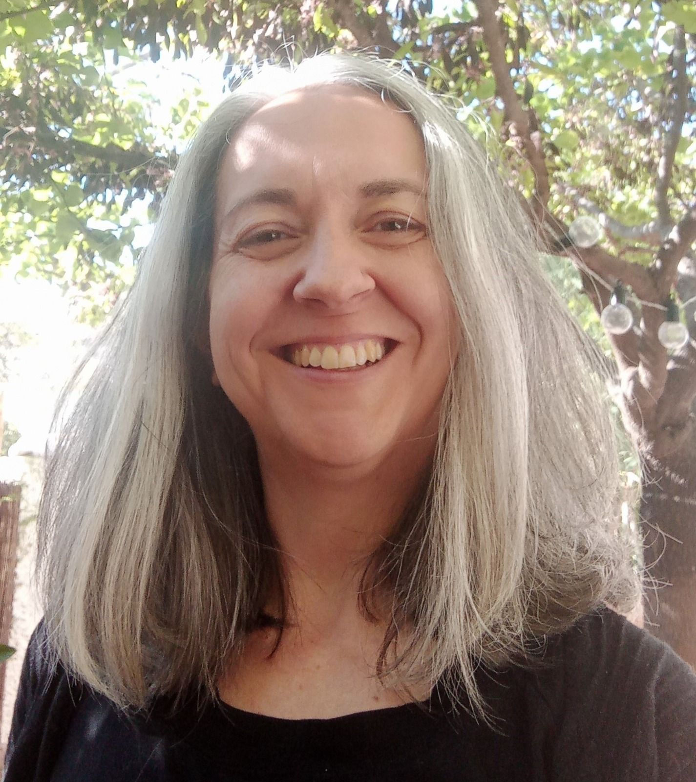 Una mujer con cabello gris sonríe delante de un árbol.