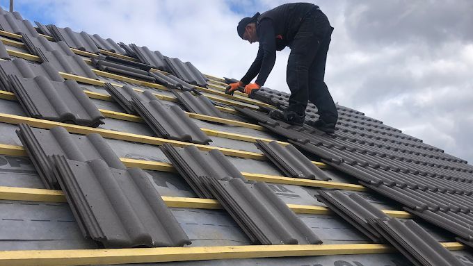 Un couvreur sur un toit avec des tuiles noires.