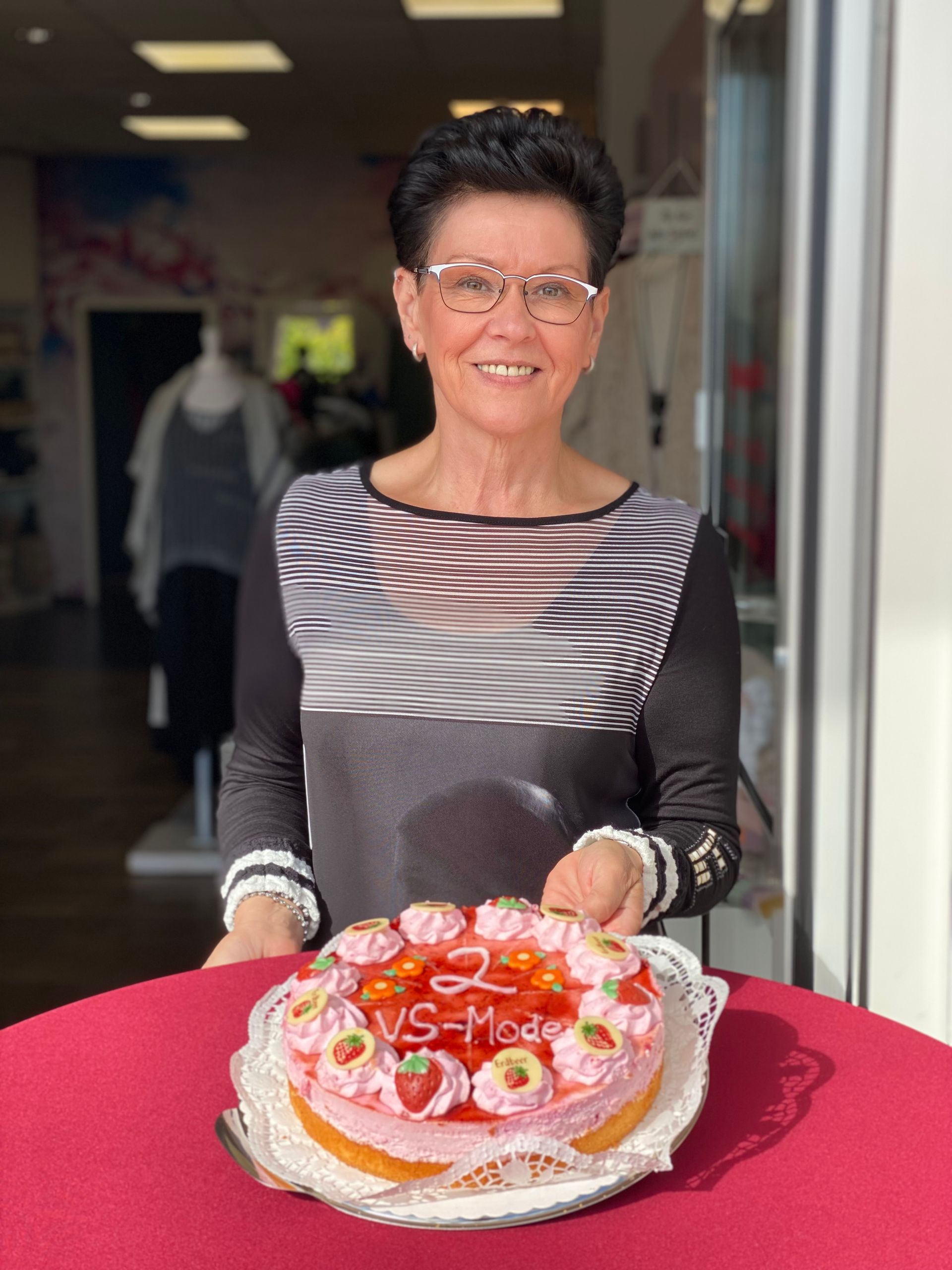Frau hält eine verzierte Torte auf einem roten Tisch in einem Innenraum