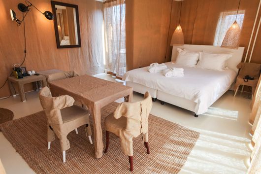 Bedroom with white linens, a double bed, and a table with chairs, all in a neutral color scheme.