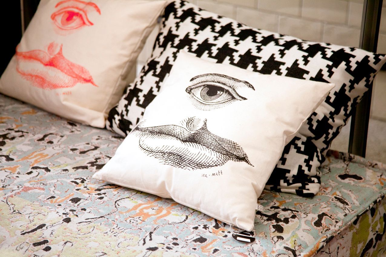 Three decorative pillows on a patterned surface. One pillow has an eye and lips graphic, the other a houndstooth pattern.